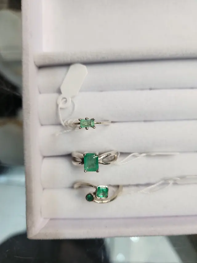 Three rings set with green emeralds in a white ring display box
