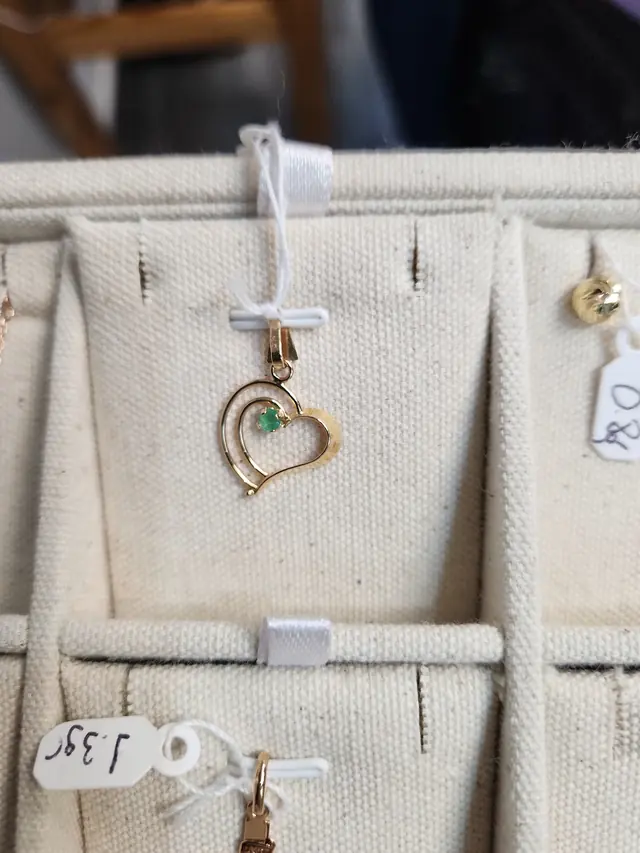 A gold open-heart pendant set with a small green stone, hanging on a canvas display roll