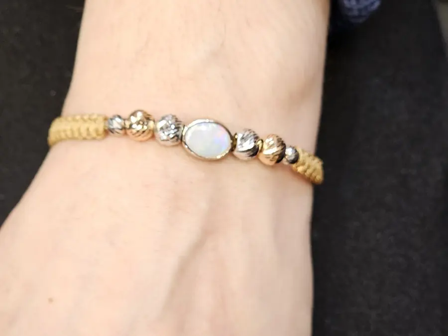 A gold and silver beaded bracelet with an opal centre stone, worn on the wrist